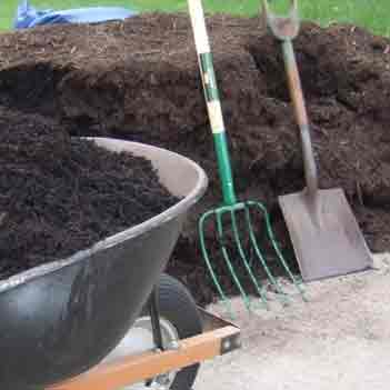 Mulch Install - Photo of a pile of mulch and a wheelbarrow full of mulch ready for spreading.   